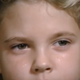 A little girl, her hair blowing wildly, glares off-camera in a shot framed from the nose up.